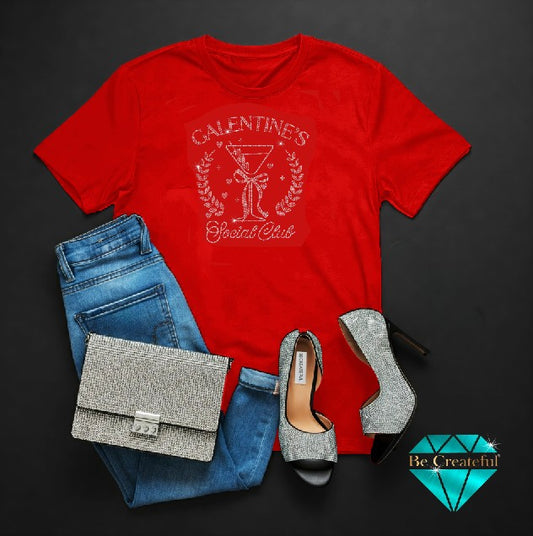 Red t-shirt with 'Galentine's Cocktail Club' design, blue jeans, gray high heels, and silver clutch on a dark background.