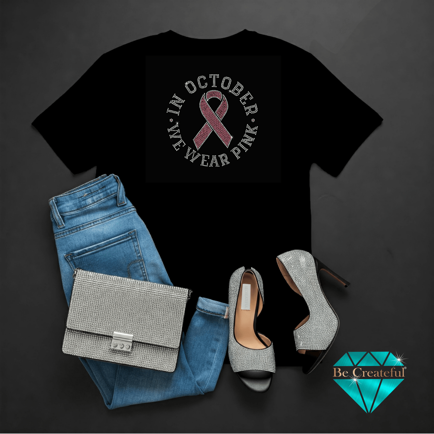 Black t-shirt with pink ribbon design, blue jeans, silver handbag, and high heels on a dark background.